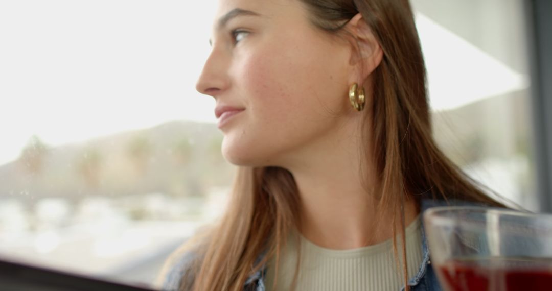 Woman Relaxing by Cafe Window Enjoying Urban View with Red Beverage