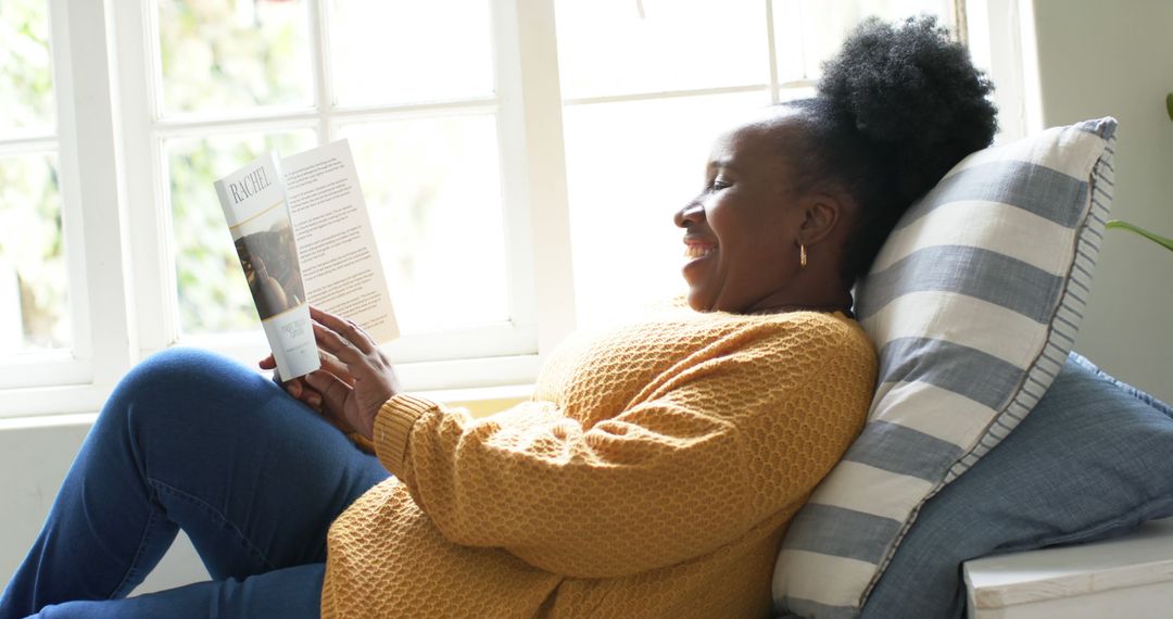 Smiling woman reading book by window on cozy afternoon - Free Images, Stock Photos and Pictures on Pikwizard.com