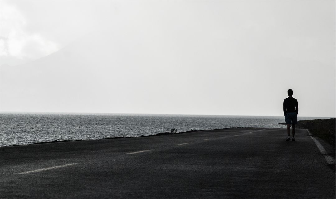 Solitary Person Walking on Coastal Road During Overcast Day - Free Images, Stock Photos and Pictures on Pikwizard.com