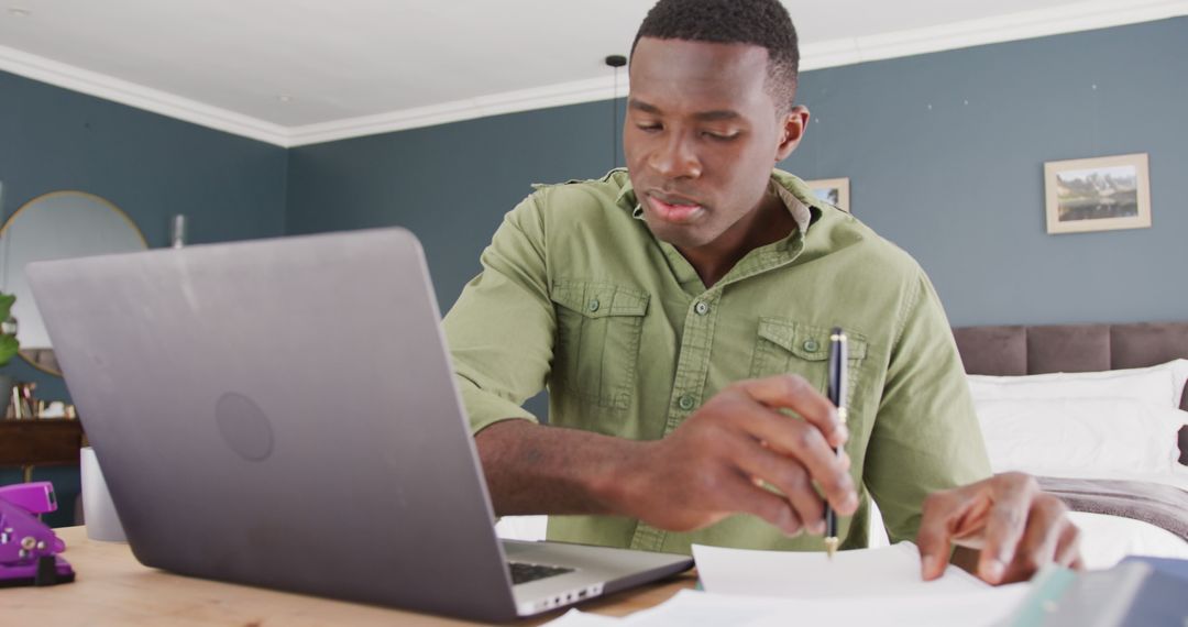 Image of african american man sitting using laptop and writing notes, working in bedroom - Free Images, Stock Photos and Pictures on Pikwizard.com