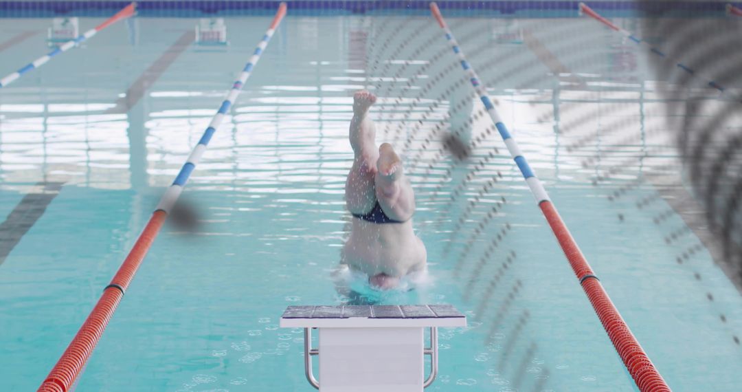 Male competitive diver executing headfirst entry from starting block in indoor lap pool