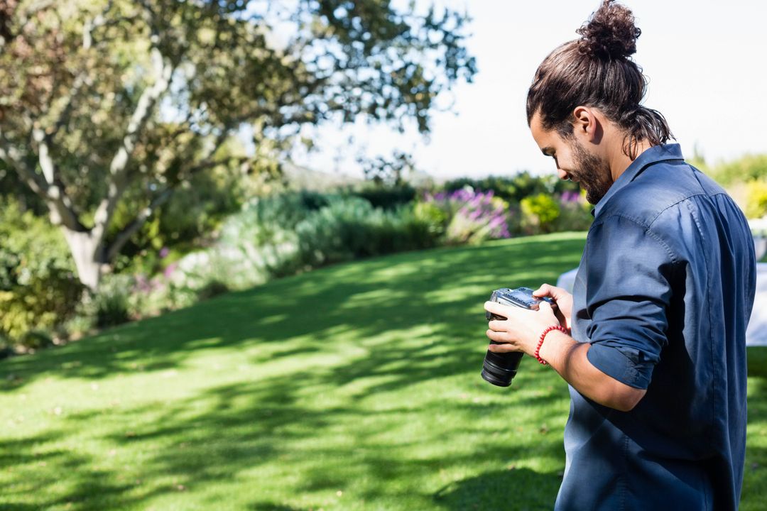 Man Adjusting DSLR Camera in Sunlit Gardens