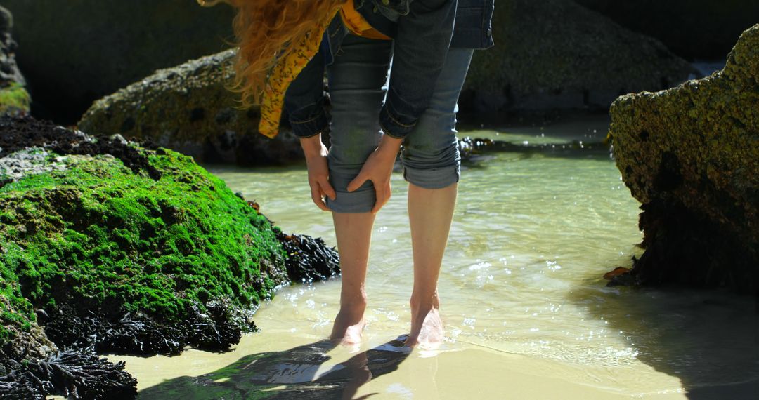 Woman Rolling Up Jeans by a Rocky Beach Shore - Free Images, Stock Photos and Pictures on Pikwizard.com