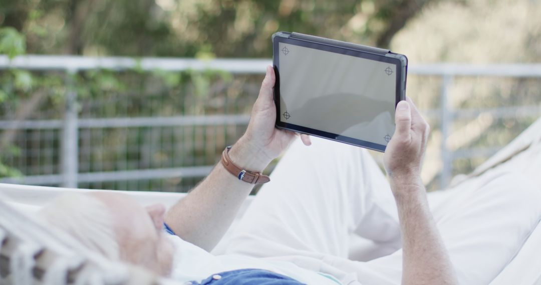 Older man relaxing on hammock and reading tablet outdoors - Free Images, Stock Photos and Pictures on Pikwizard.com