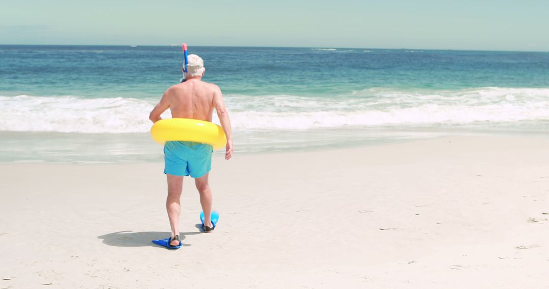 Senior Man Walking on Beach with Snorkeling Gear and Inner Tube - Free Images, Stock Photos and Pictures on Pikwizard.com