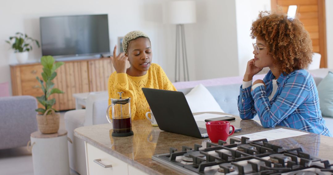 Two Women Discussing Work at Kitchen Counter with Laptop and Coffee - Free Images, Stock Photos and Pictures on Pikwizard.com