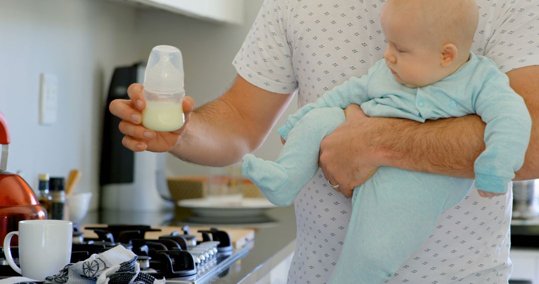 Father Holding Baby in Kitchen While Preparing Bottle Feeding - Free Images, Stock Photos and Pictures on Pikwizard.com