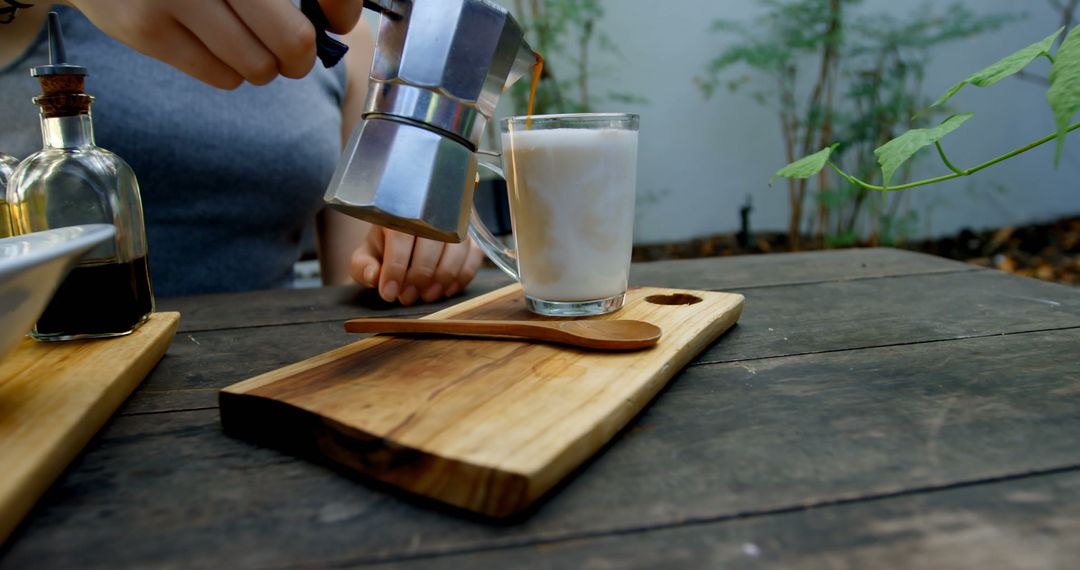 Person Pouring Coffee into Latte Glass Outdoors on Rustic Wooden Table - Free Images, Stock Photos and Pictures on Pikwizard.com