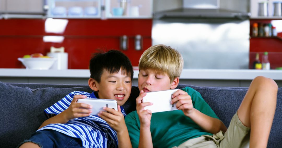 Two Children Playing Mobile Games on Sofa in Modern Kitchen - Free Images, Stock Photos and Pictures on Pikwizard.com