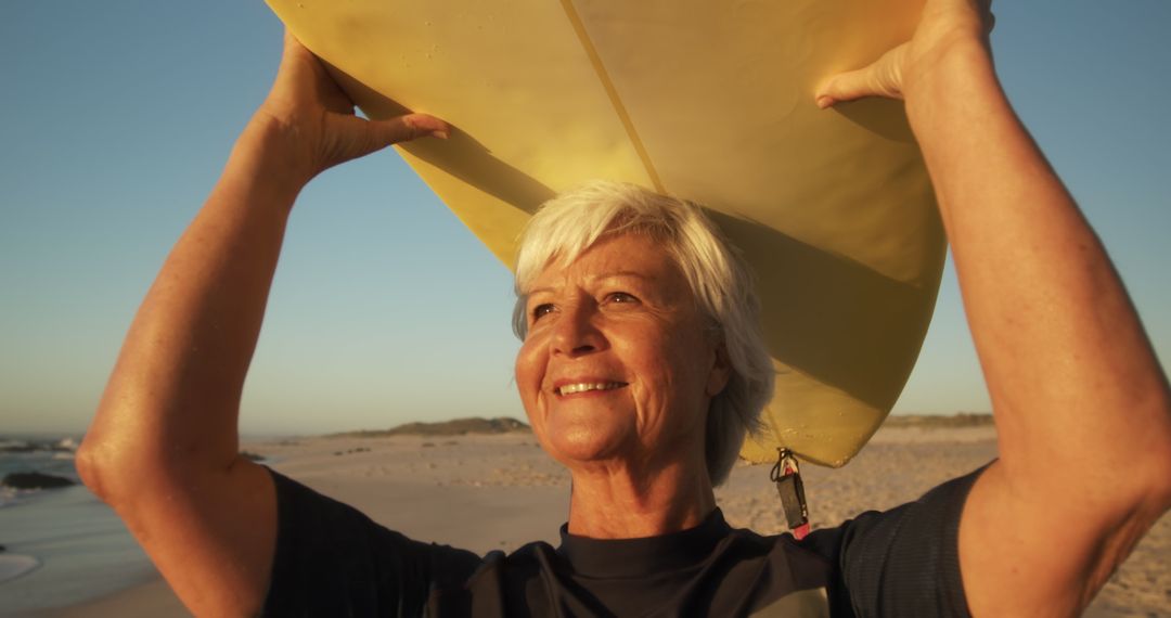 Senior Woman Carrying Surfboard On Beach at Sunset - Free Images, Stock Photos and Pictures on Pikwizard.com