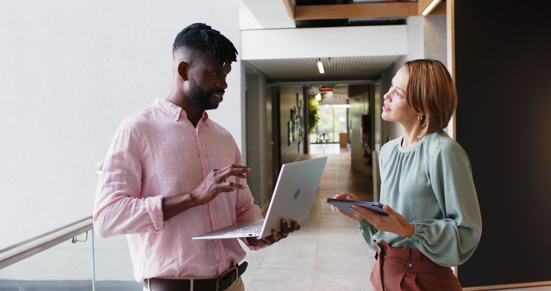 Colleagues Collaborating in Office Hallway with Laptop and Tablet