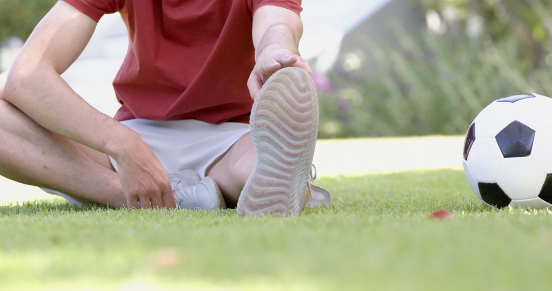 Active Man Stretching on Lawn with Soccer Ball Drinking In Sunlight