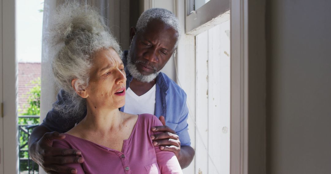 Senior Couple Comforting Each Other Looking Out Window at Home