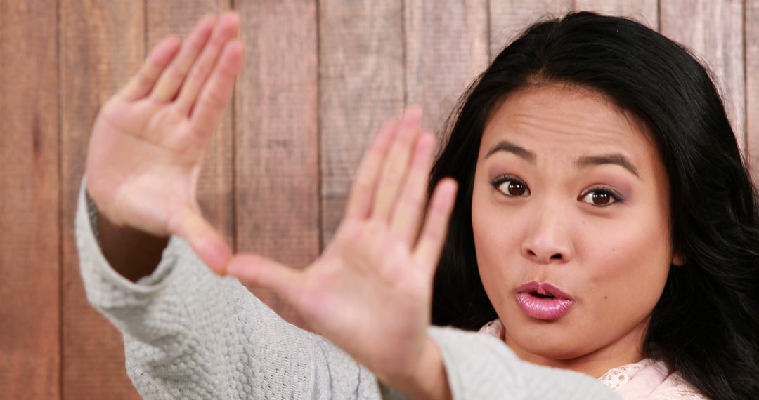 Woman Framing Face with Hands Gesture Against Wooden Wall - Free Images, Stock Photos and Pictures on Pikwizard.com