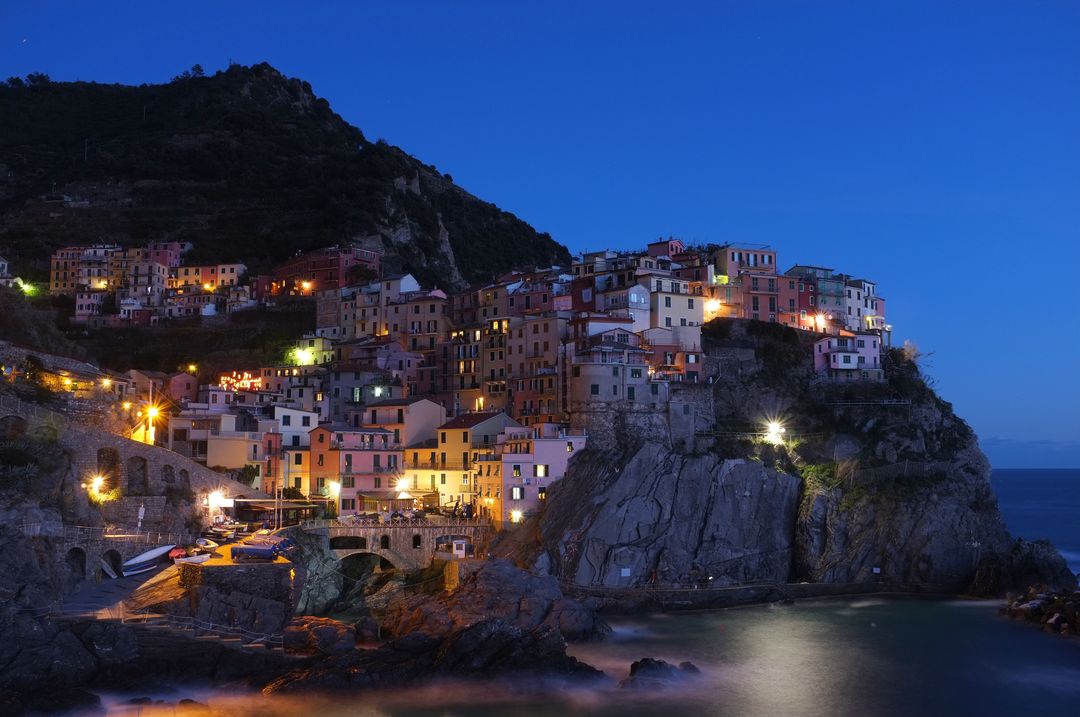 Manarola Village Illuminated at Dusk on Cliffside by Sea - Free Images, Stock Photos and Pictures on Pikwizard.com