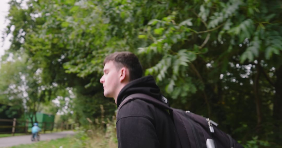 Young Man Running Through Green Park with Backpack