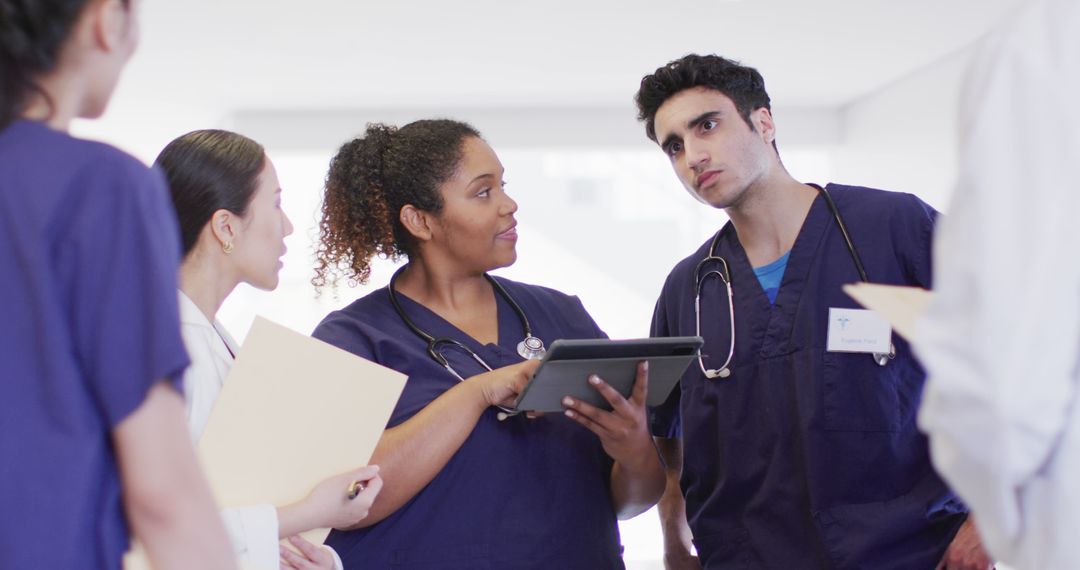 Image of diverse group of male and female doctors looking at tablet talking in hospital corridor - Free Images, Stock Photos and Pictures on Pikwizard.com