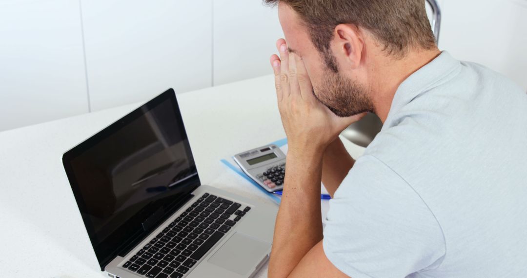 Upset man doing his accounting with a laptop in the kitchen - Free Images, Stock Photos and Pictures on Pikwizard.com