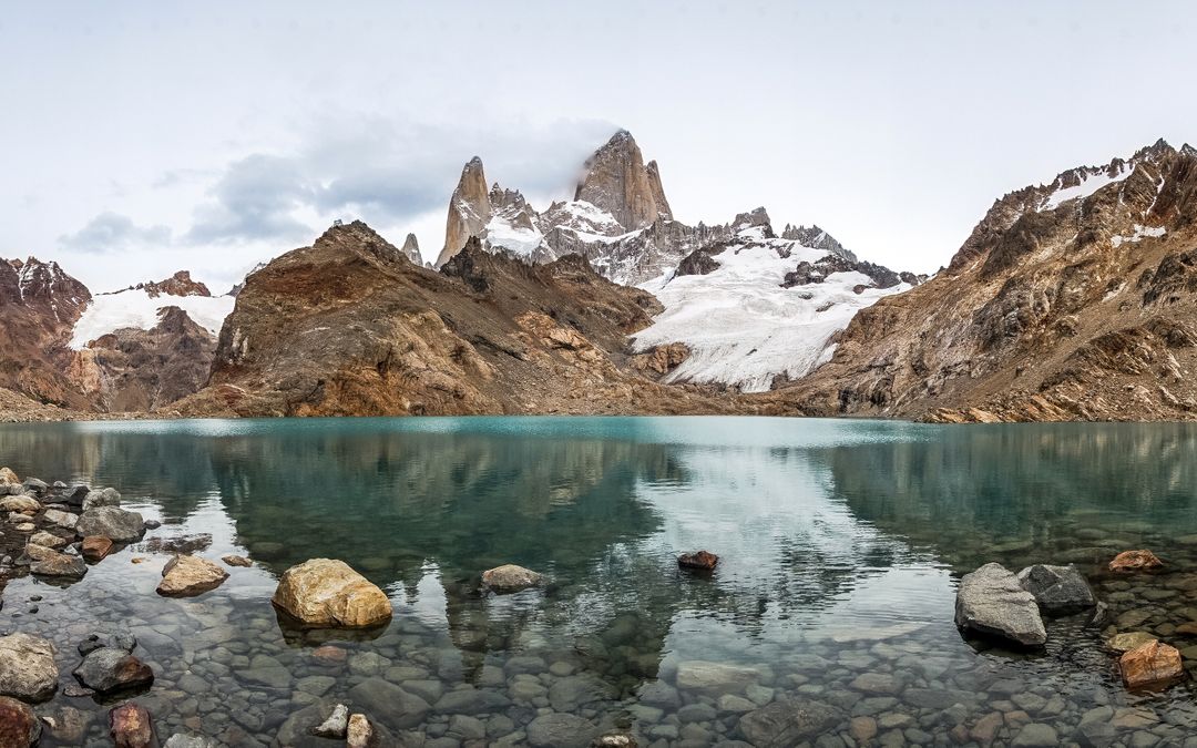 Panoramic View of Fitz Roy Mountains with Tranquil Lake and Rocky Shore - Free Images, Stock Photos and Pictures on Pikwizard.com