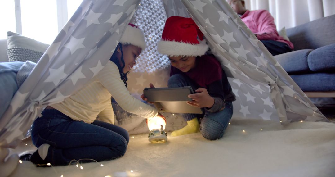 Children Enjoying Christmas Tent Playtime with Tablet and Fairy Lights - Free Images, Stock Photos and Pictures on Pikwizard.com