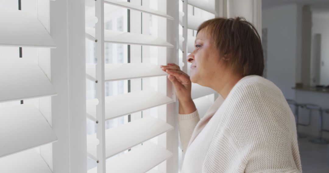 Woman Gazing Out Window with Shutters in Cozy Home Setting - Free Images, Stock Photos and Pictures on Pikwizard.com