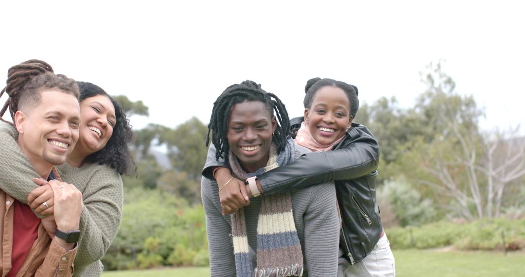 Diverse friends piggybacking and laughing on lawn, hugging and enjoying outdoors