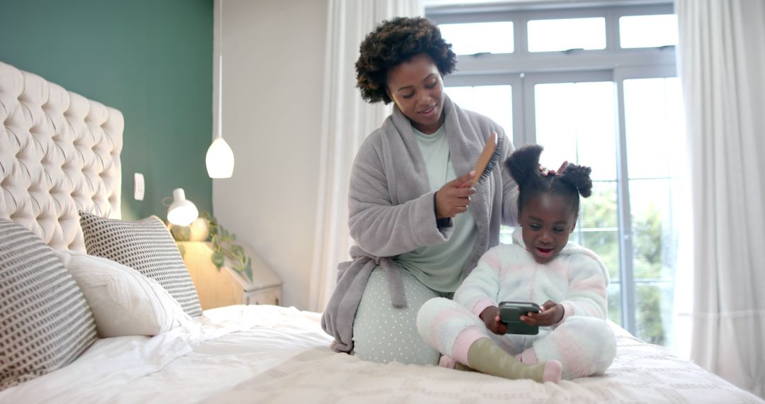 Mother Combing Daughter's Hair While She Uses Smartphone in Cozy Bedroom - Free Images, Stock Photos and Pictures on Pikwizard.com