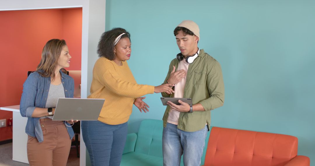 Diverse Team Collaborating in Colorful Office Lounge Using Tablet and Laptop