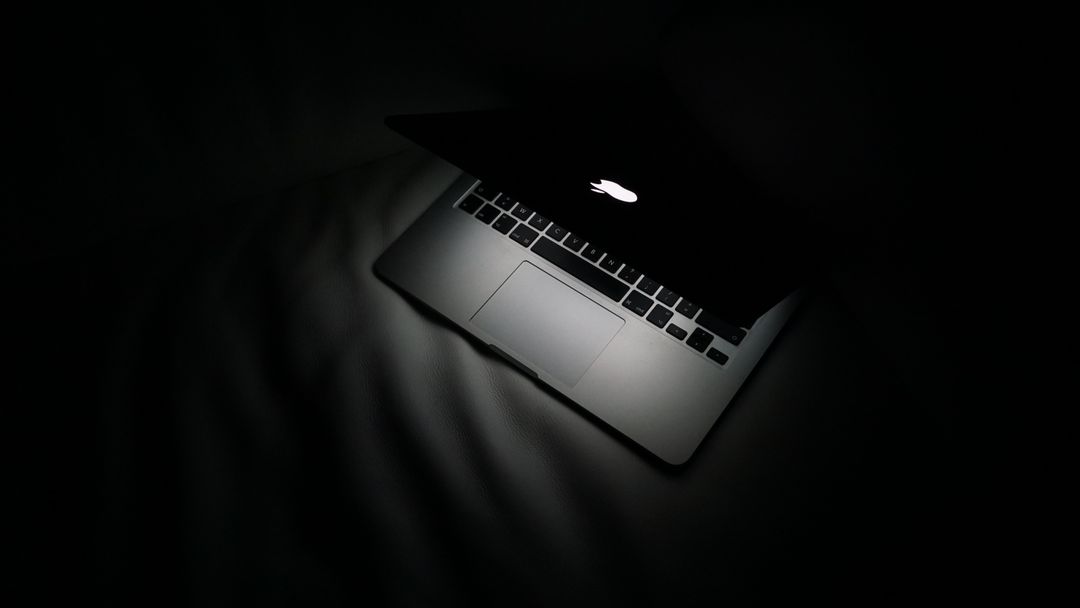 Partially Open Laptop in Dark Room with Glowing Apple Logo - Free Images, Stock Photos and Pictures on Pikwizard.com