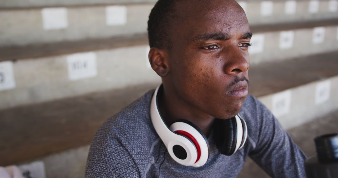 Young Man wearing Headphones Sitting in Bleachers Showing Determination - Free Images, Stock Photos and Pictures on Pikwizard.com