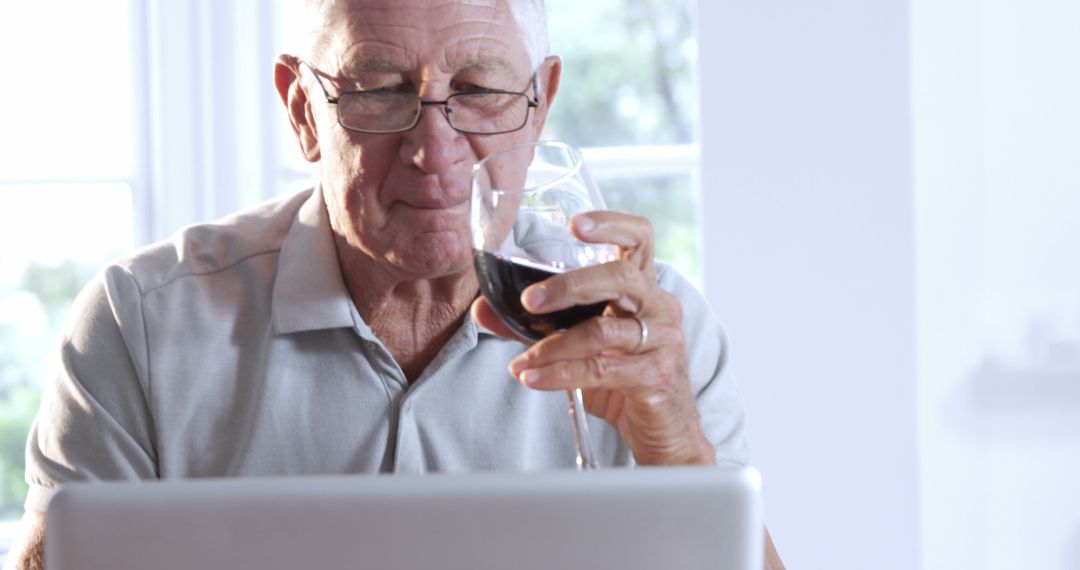 Elderly man enjoying red wine while using laptop at home - Free Images, Stock Photos and Pictures on Pikwizard.com