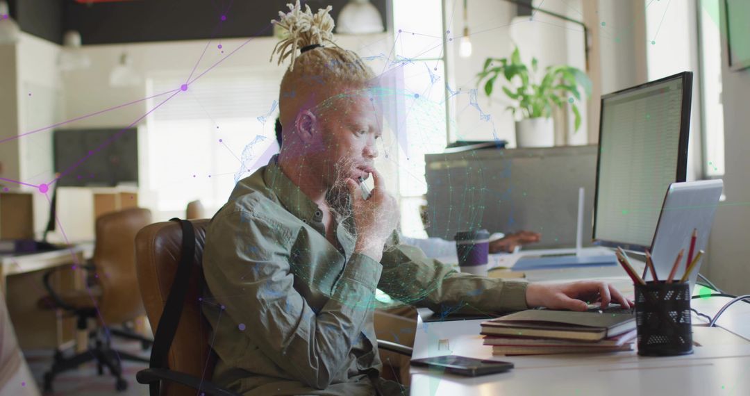 Focused coworking professional typing at dual-screen desk with laptop, notebooks and coffee