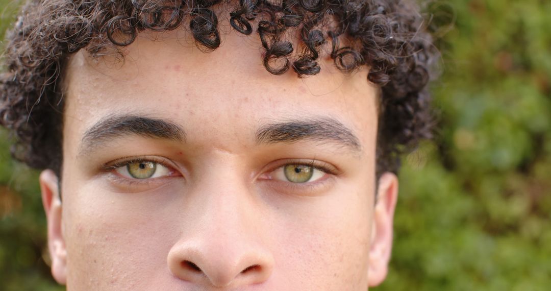 Curly-haired young man's serious face with captivating green eyes - Free Images, Stock Photos and Pictures on Pikwizard.com