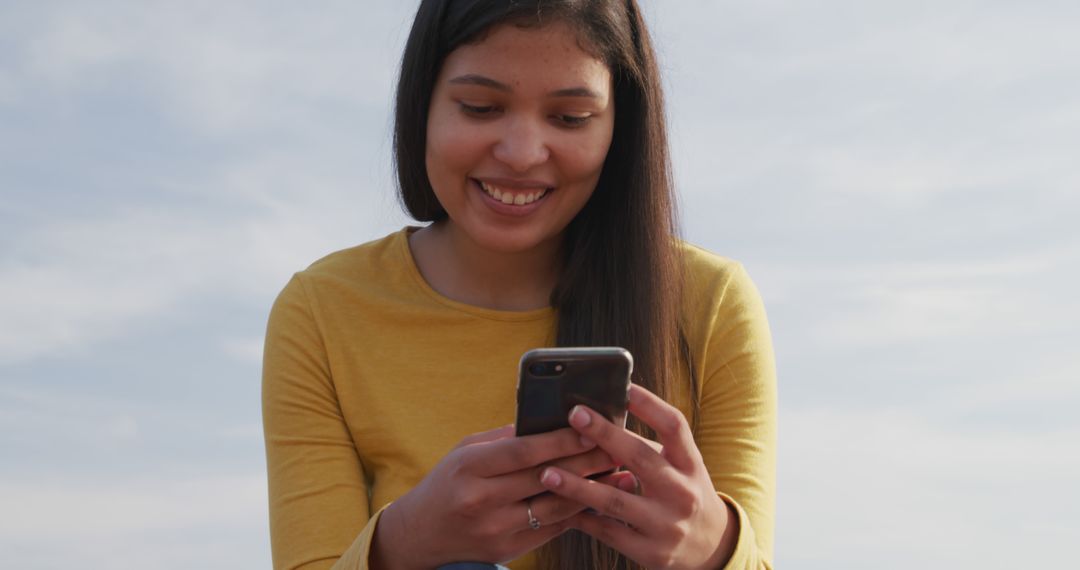 Smiling Young Woman Engaging with Smartphone Outdoors - Free Images, Stock Photos and Pictures on Pikwizard.com