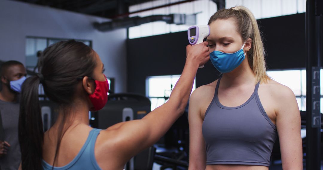 Woman checking another woman's temperature at gym wearing face masks - Free Images, Stock Photos and Pictures on Pikwizard.com