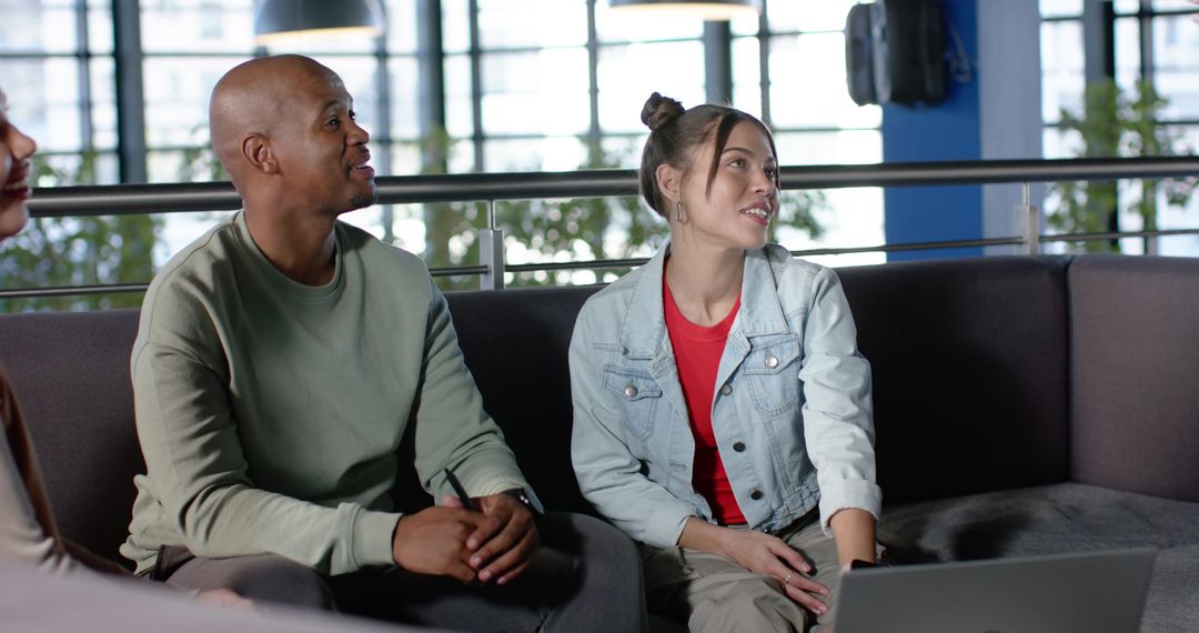 Collaborating diverse coworkers in modern office lounge using laptop and discussing ideas