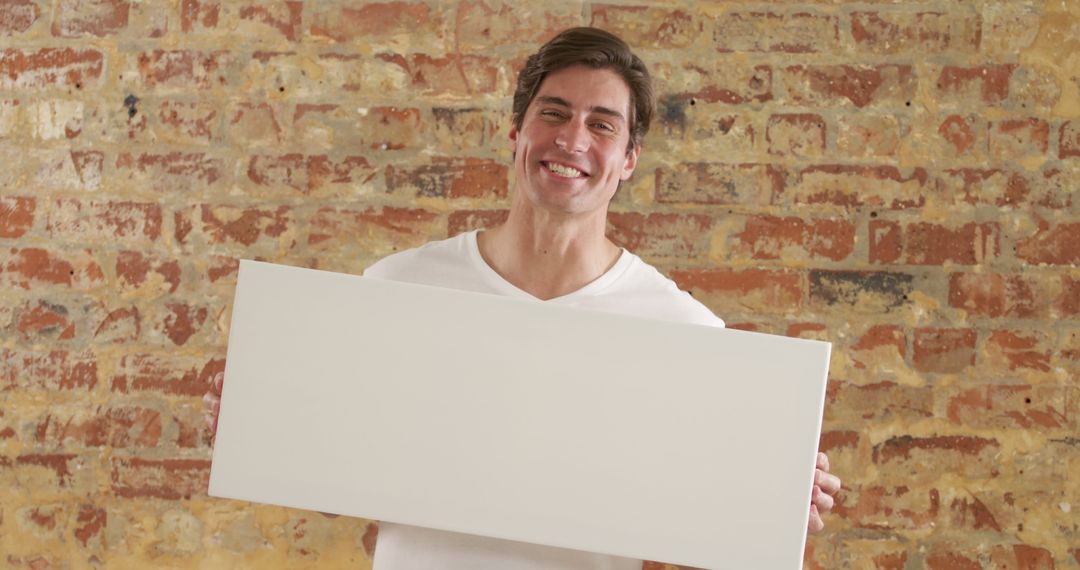 Smiling Man Holding Blank White Sign Against Brick Wall - Free Images, Stock Photos and Pictures on Pikwizard.com