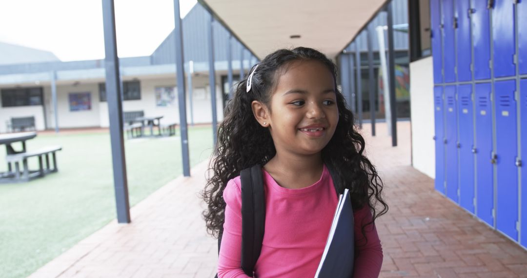 Young Hispanic Girl Smiling in School Courtyard Holding Notebook