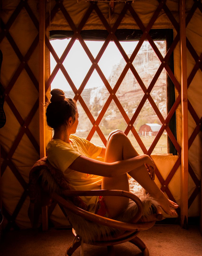 Woman Gazing Through Yurt Window at Mountain View During Golden Hour
