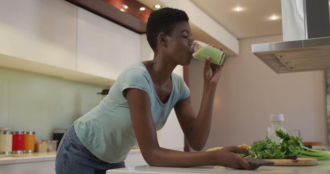 Woman Drinking Green Smoothie While Preparing Vegetables in Modern Kitchen - Free Images, Stock Photos and Pictures on Pikwizard.com