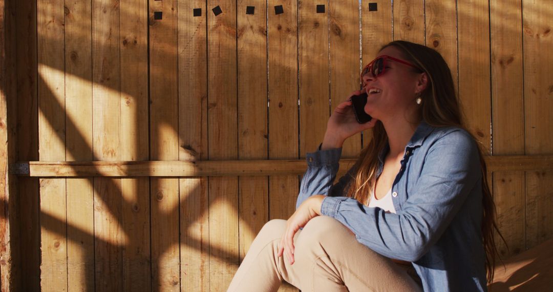 Woman in Sunglasses Talking on Phone Outdoors by Wooden Fence - Free Images, Stock Photos and Pictures on Pikwizard.com