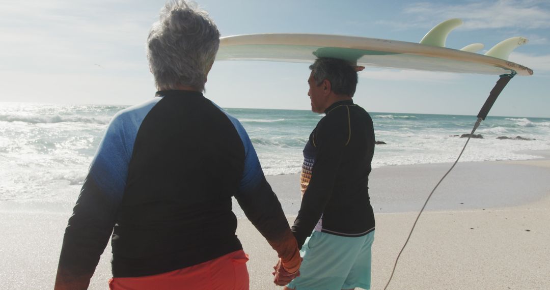 Senior Couple Walking on Beach with Surfboard During Retirement
