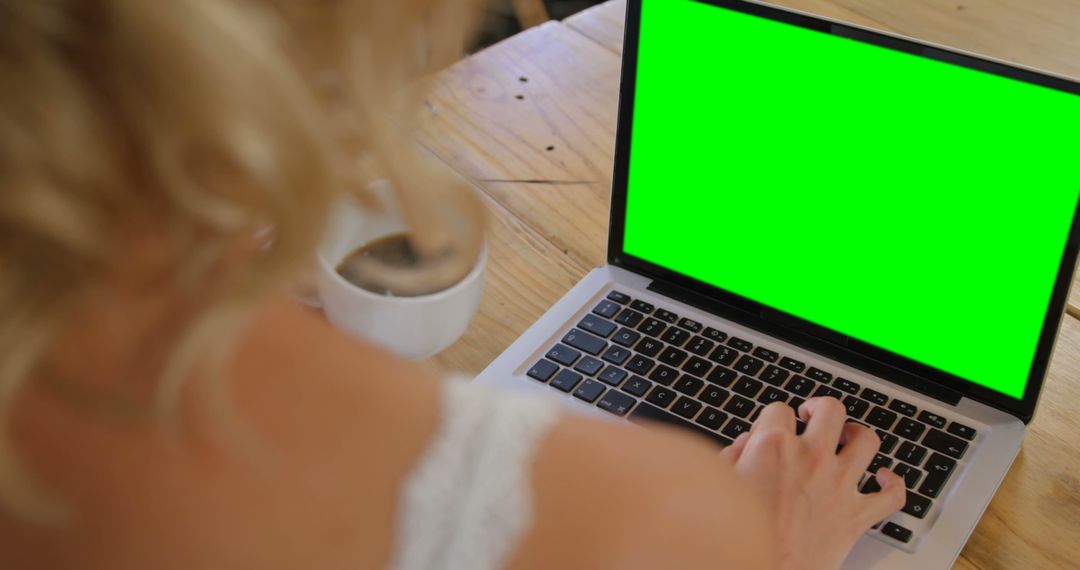 Person Using Laptop with Green Screen while Drinking Coffee at Wooden Table - Free Images, Stock Photos and Pictures on Pikwizard.com