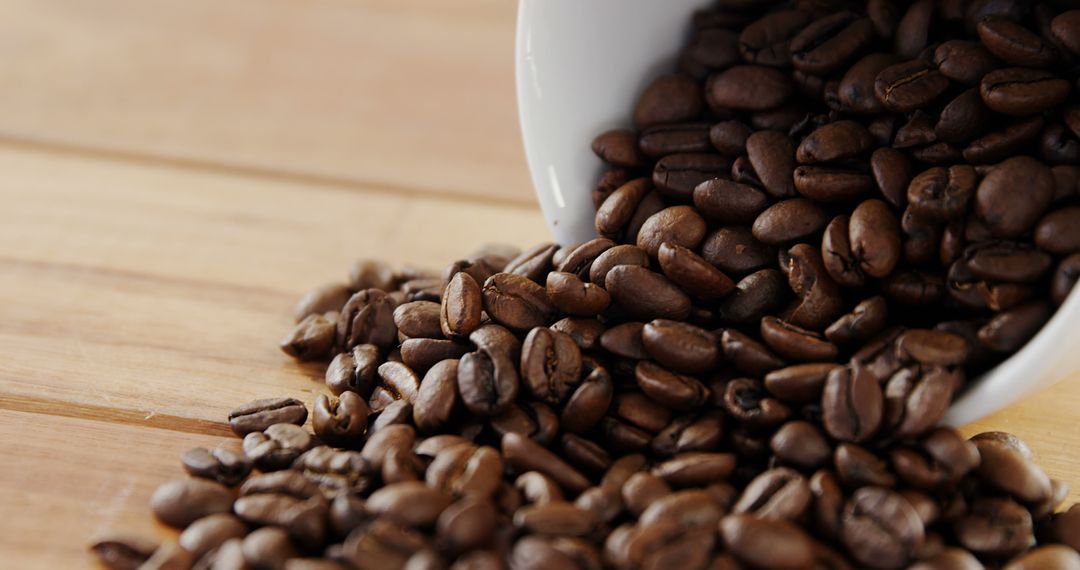 Coffee beans spilling from white cup on wooden surface - Free Images, Stock Photos and Pictures on Pikwizard.com