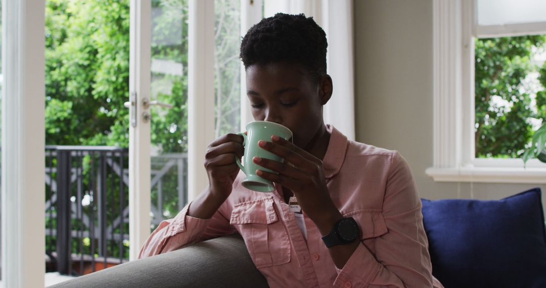 Afro-American woman drinking coffee on cozy couch in sunlit living room - Free Images, Stock Photos and Pictures on Pikwizard.com