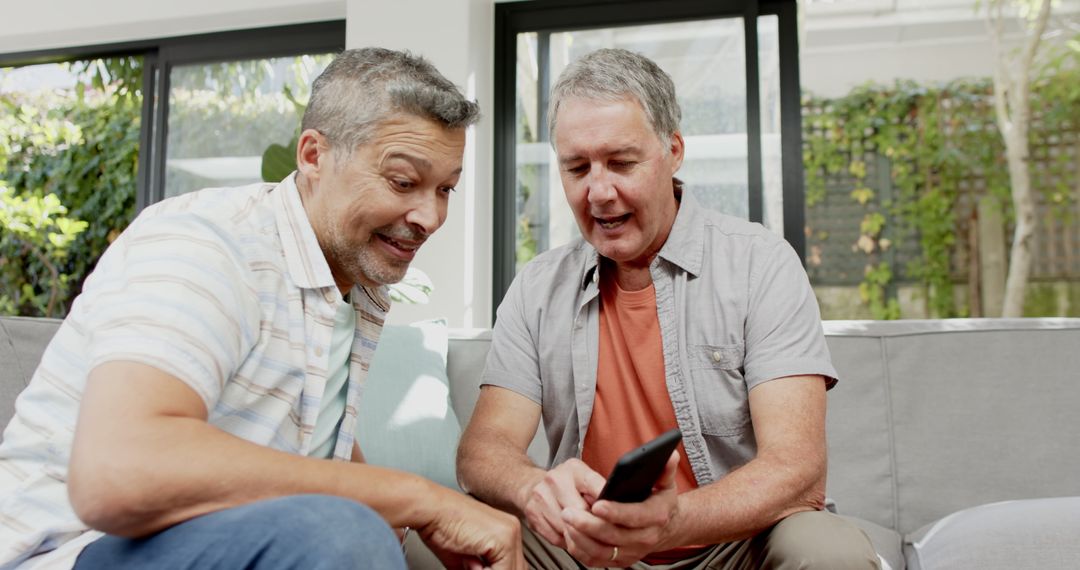 Two friends relaxing on sofa examining smartphone together