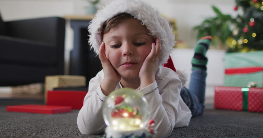 Child Wearing Santa Hat Admiring Christmas Snow Globe - Free Images, Stock Photos and Pictures on Pikwizard.com