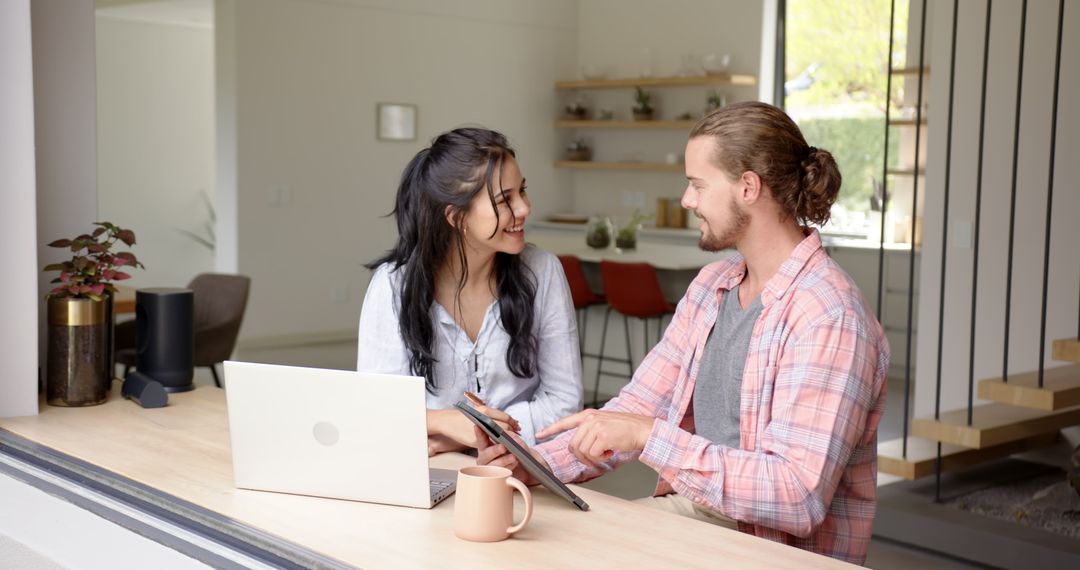 Cheerful Couple Using Laptop and Tablet in Modern Kitchen