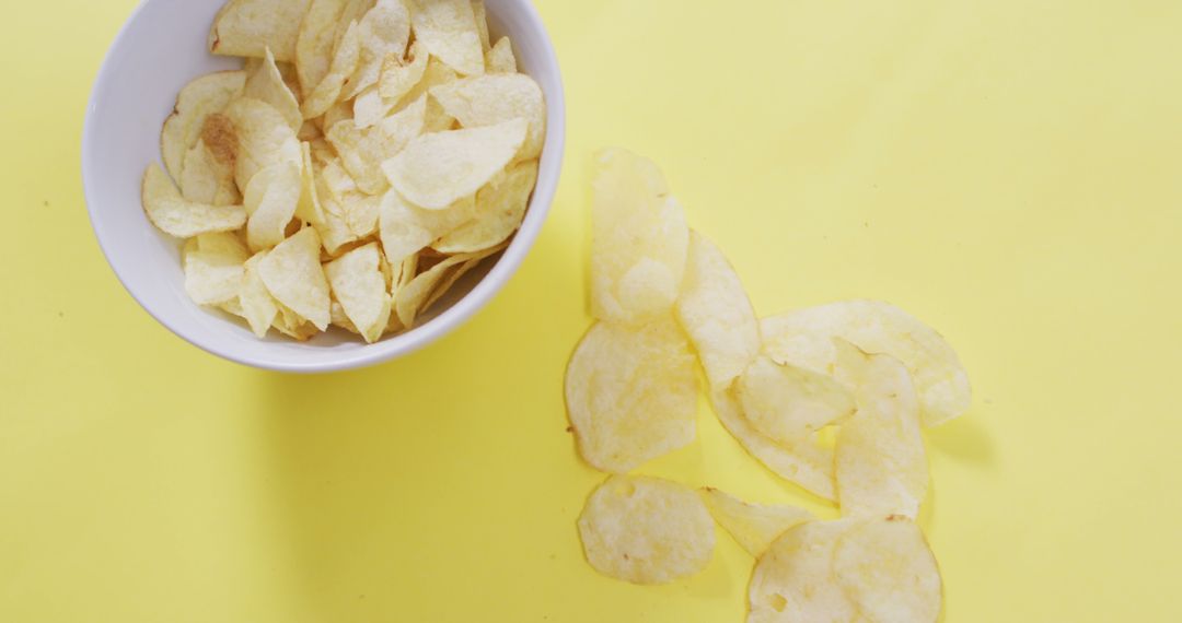 Close up of potato chips falling in a bowl on yellow surface - Free Images, Stock Photos and Pictures on Pikwizard.com
