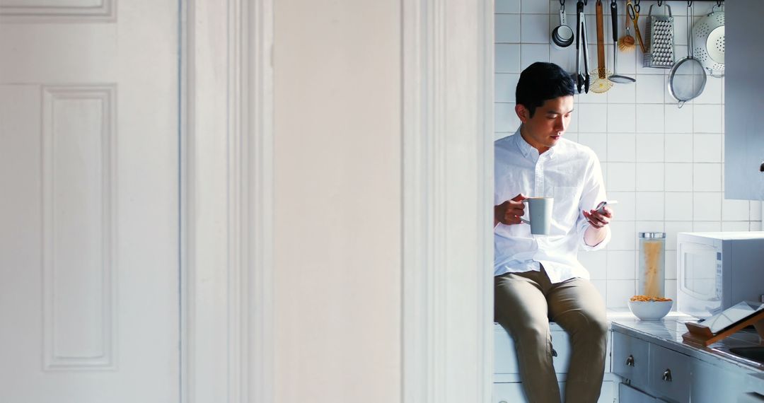 Young Man Holding Coffee Mug Sitting in Kitchen - Free Images, Stock Photos and Pictures on Pikwizard.com